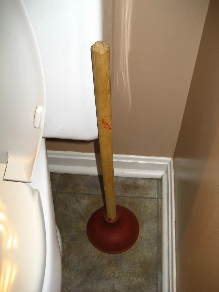 Plunger with a wooden handle standing on the floor beside a bathroom wall