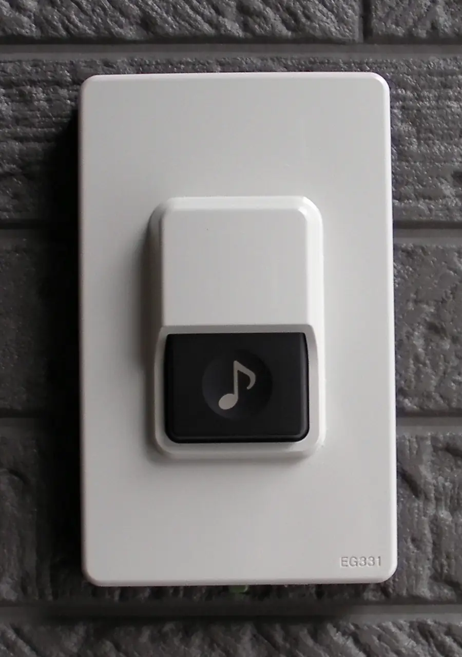 White rectangular doorbell button with a music note on a dark wall