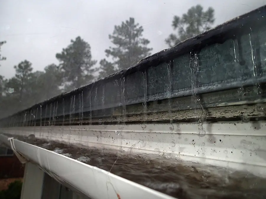 Roof gutter filled with rainwater and overflowing during a storm
