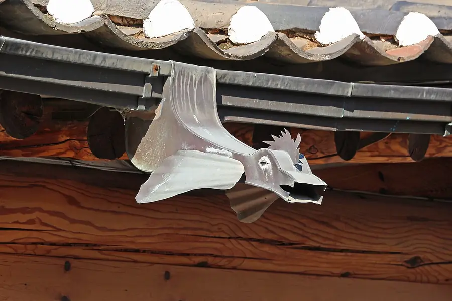 Metal gutter with a decorative fish-shaped spout under a tile roof edge