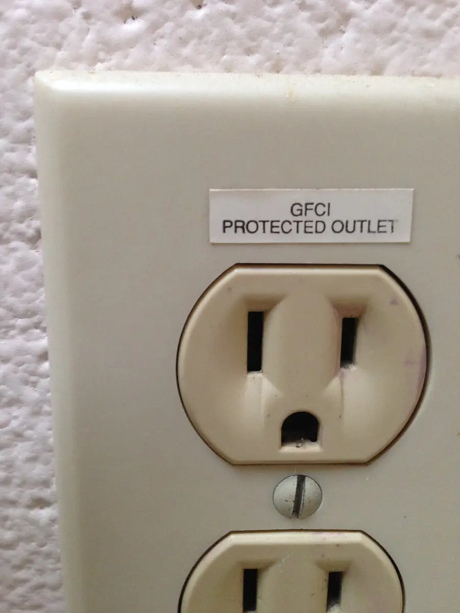 Beige duplex outlet labeled GFCI protected outlet on a textured wall