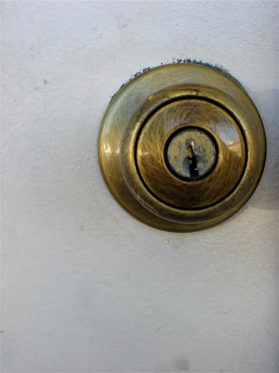 Brass deadbolt key cylinder set into a white door, seen up close
