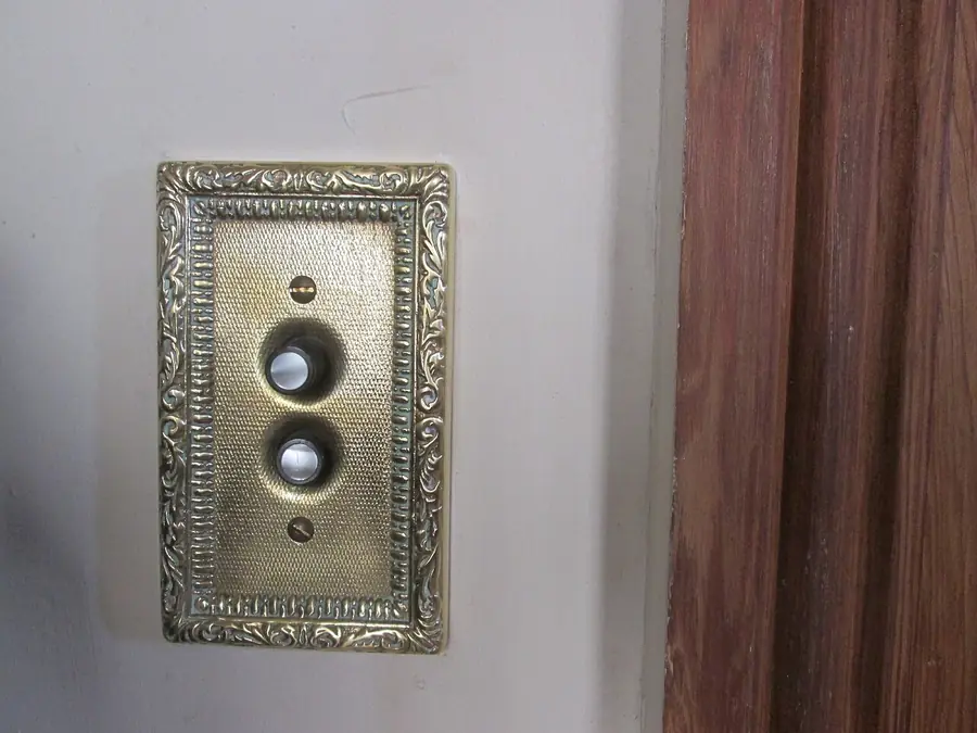 Vintage push-button light switch behind an ornate brass plate in an older home