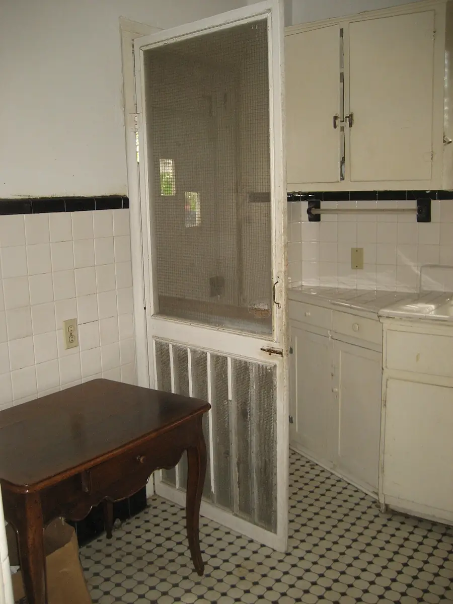 Wood-framed screen door with a lower grille opening from a tiled kitchen
