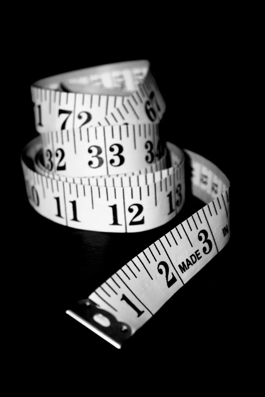 Coiled cloth tape measure with black numbers on a black background