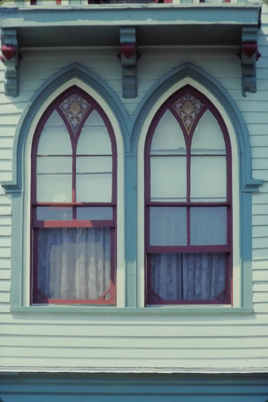 Two tall arched windows with green trim on a historic wood house