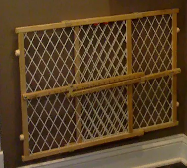 Wooden pressure baby gate with white mesh stored against a hallway wall