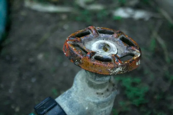 靠近地面的旧户外水龙头上生锈的圆形手轮
