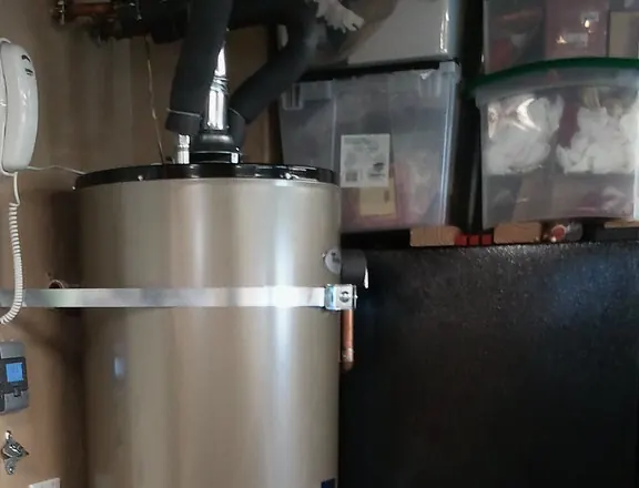 Top of a gas water heater in a garage with flue pipe and seismic strap