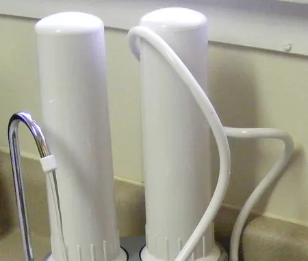 Two white drinking water filter housings with a small spout beside a kitchen sink