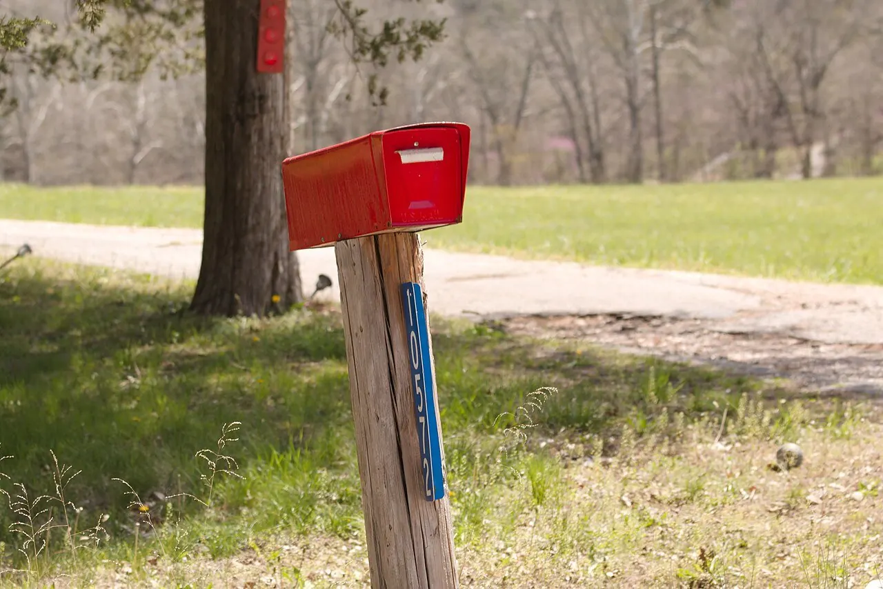 Red mailbox on a wooden post beside a road