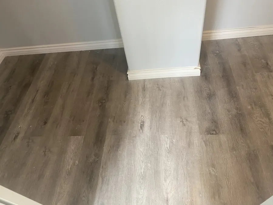 Corner where white baseboard meets a wall return over vinyl plank