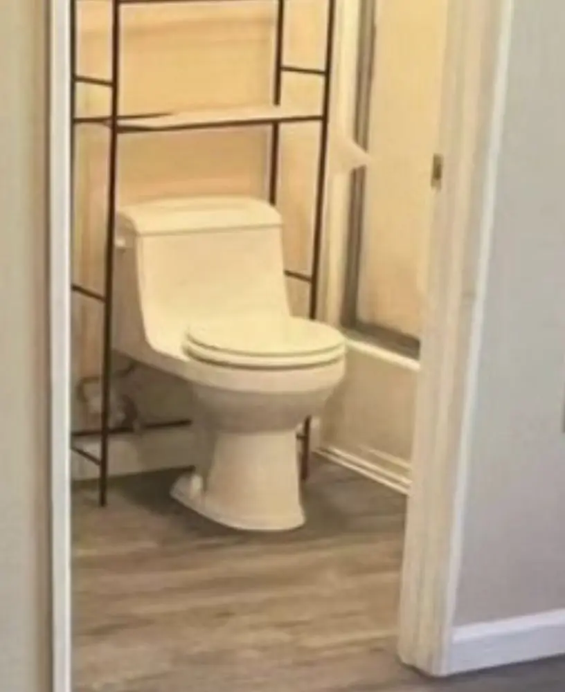 One-piece white toilet in a small bathroom under an over-the-toilet storage shelf
