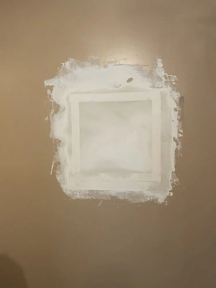 Square drywall patch with fresh joint compound around the edges