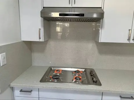 Stainless range hood mounted above a cooktop with a new backsplash